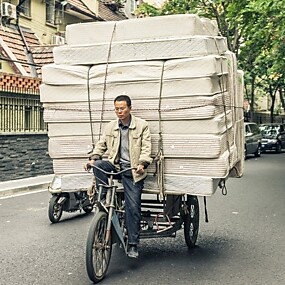 Velofahrer in asiatischem Land, der Matratzen auf Velo transportiert